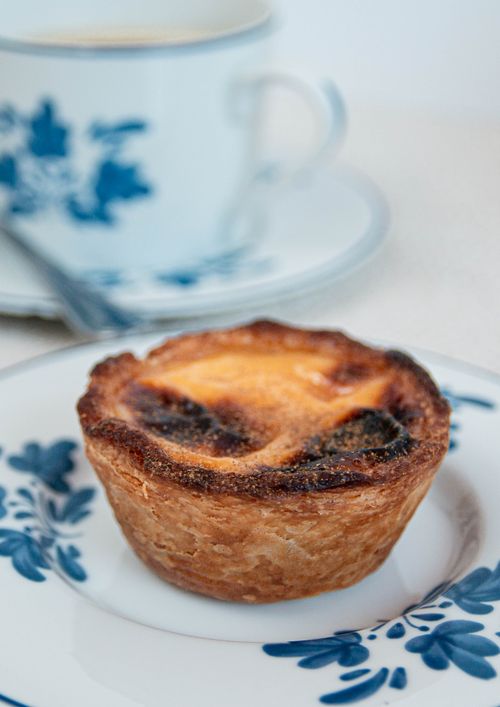 Free Close-up of a traditional Portuguese egg tart on a decorative plate with coffee background. Stock Photo