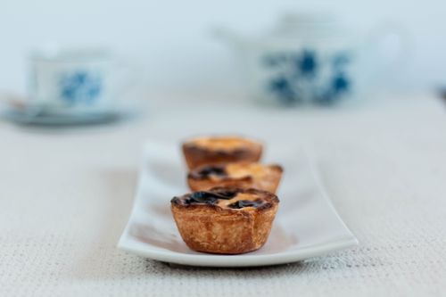 Free Three Portuguese egg tarts on a ceramic tray with a teapot background. Stock Photo