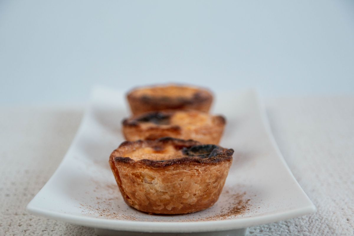 Three custard tarts dusted with cinnamon on a white plate — photo by Regina Ferraz on Pexels