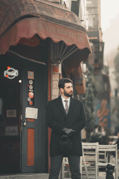 Free Man in suit standing outside a café, exuding urban charm and style. Stock Photo