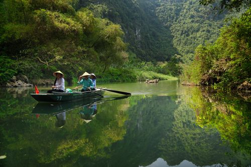 Free Women in hats rowing a boat on a serene river surrounded by lush greenery and mountains. Stock Photo