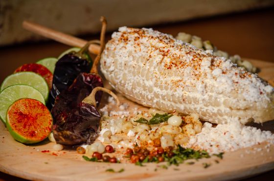 Grilled white corn coated in cotija and chile powder with limes and dried chiles