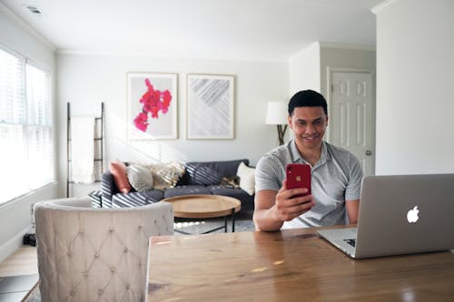 Free A Man Using a Smartphone and a Laptop Stock Photo