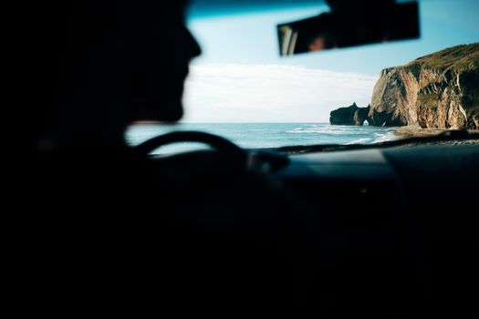Silhouette of a person driving by the ocean with a stunning cliffside view.
