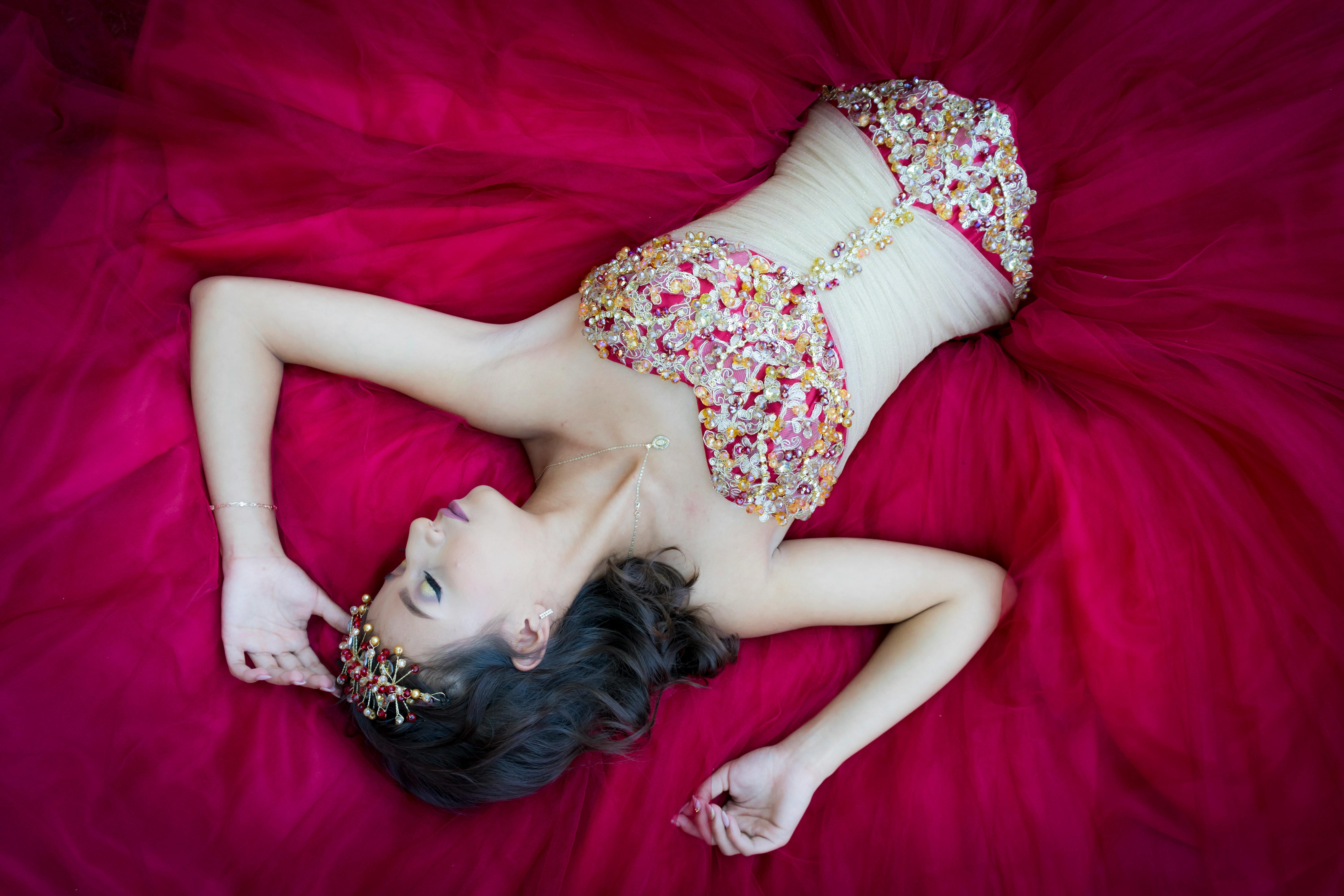 Beautiful woman in a luxurious red dress with ornate bodice, lying gracefully.