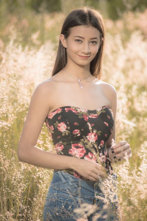 Free Smiling woman in a floral tube top standing in a sunny field. Stock Photo