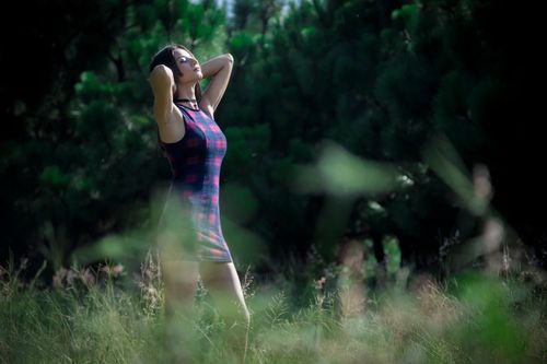 Free A woman in a dress posing confidently in a lush outdoor setting with sunlight filtering through trees. Stock Photo