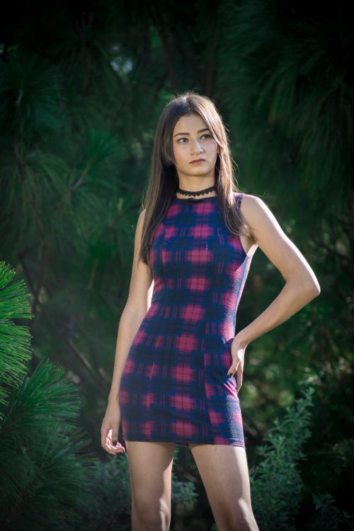 Free Confident woman posing in a plaid dress surrounded by lush greenery. Stock Photo