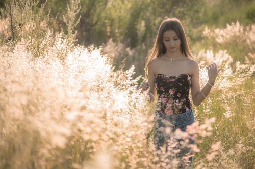 Free A young woman in a floral top walking through a serene sunlit field. Stock Photo