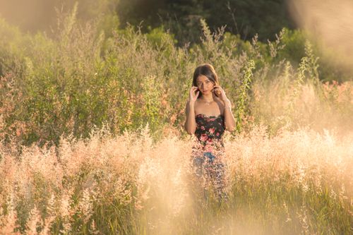 Free A young woman stands gracefully among sunlit wildflowers, evoking a serene summer vibe. Stock Photo