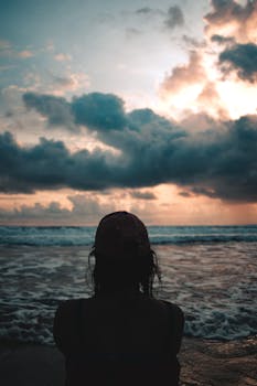 A woman silhouette against a dramatic beach sunset with clouds.