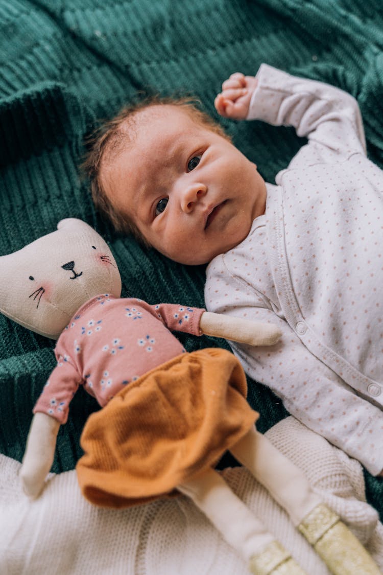 Baby Lying Next To Plush Doll