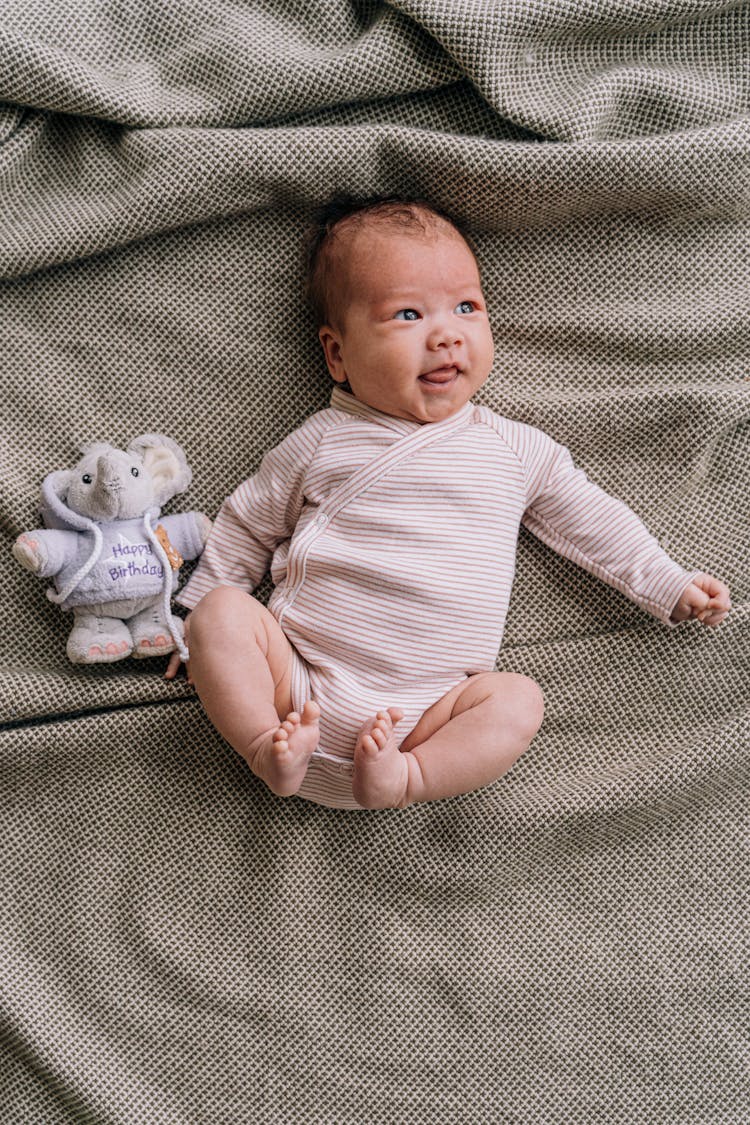 Baby In Striped Pink And White Onesie Lying On A Blanket