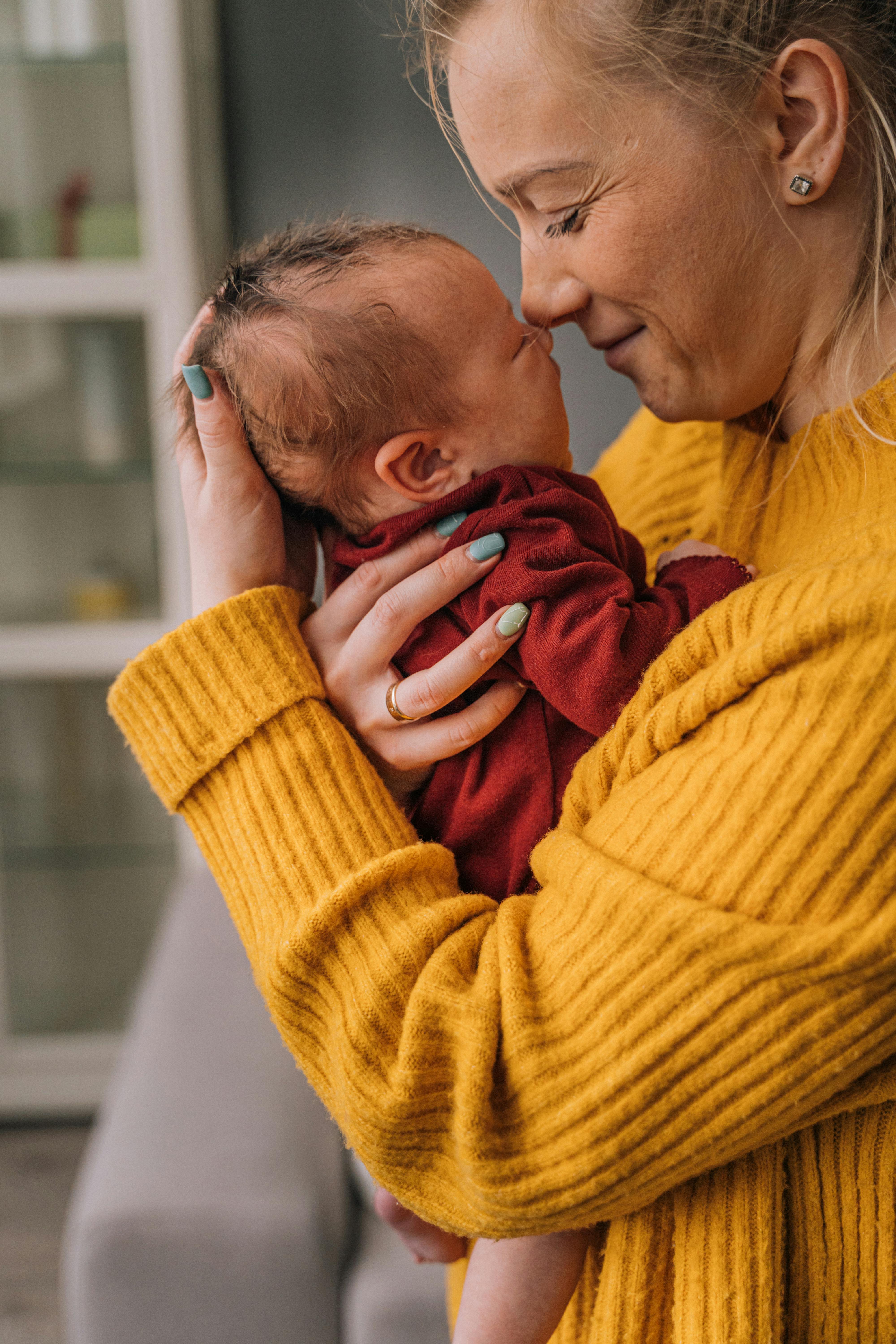 woman in yellow sweater kissing an infant in red sweater