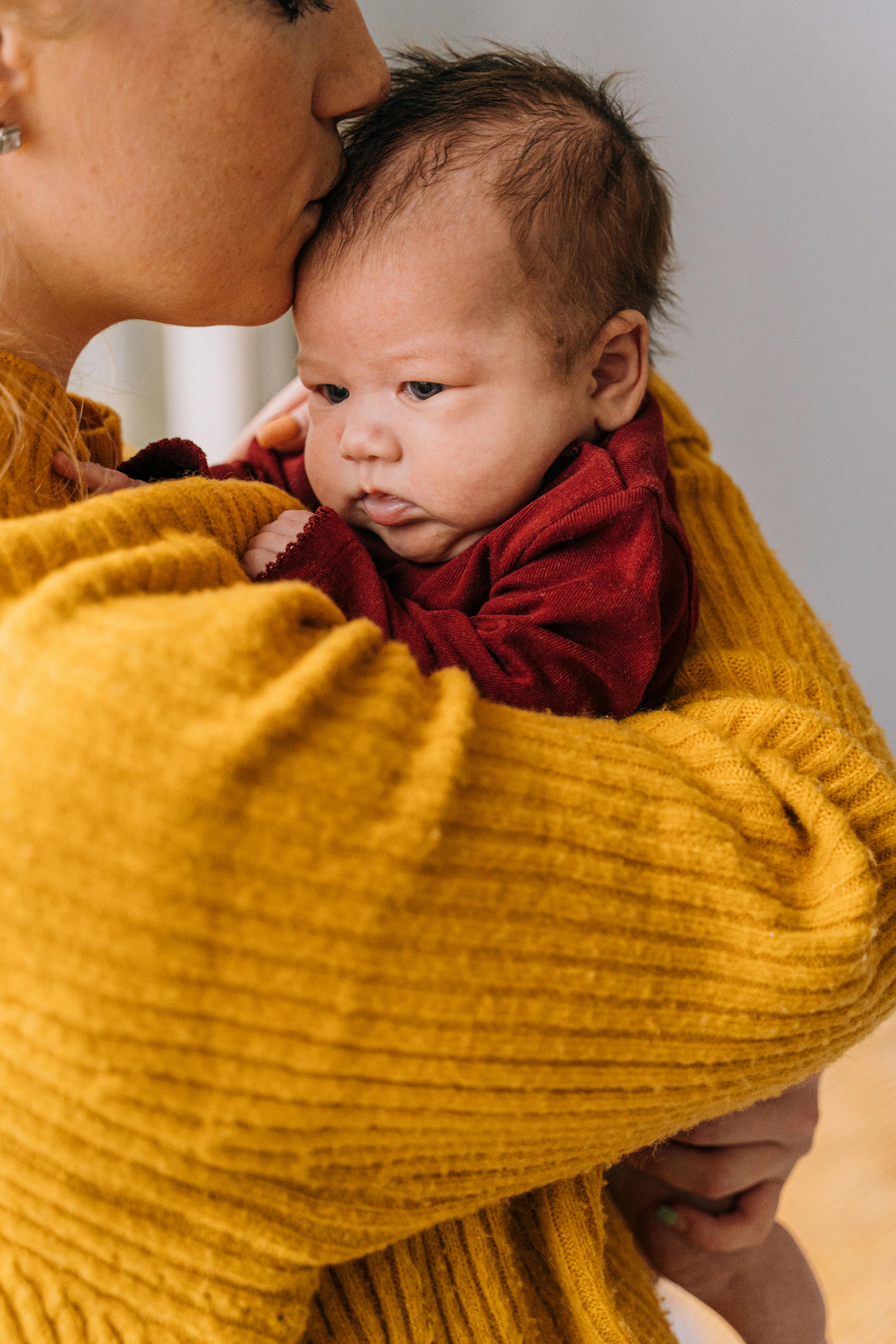 A Woman in Yellow Knit Sweater Carrying Baby in Red Shirt Free