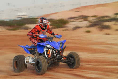 Man in Red Outfit Riding An ATV on Brown Sand