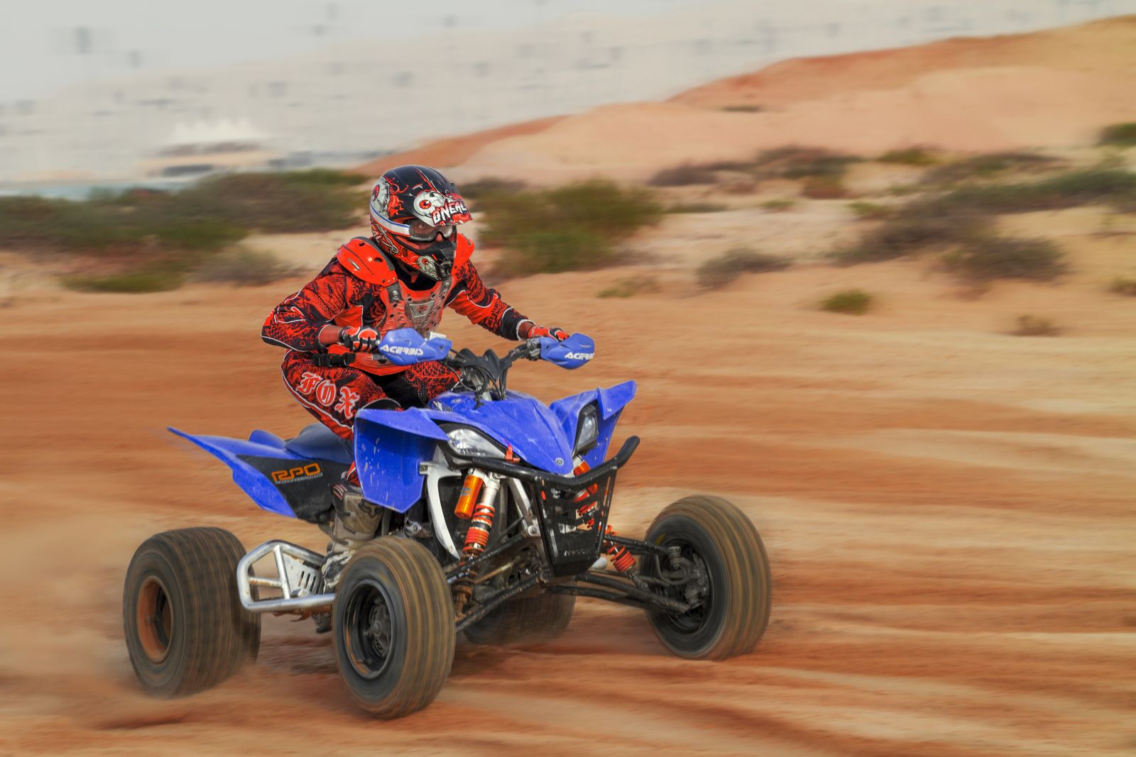 Rider in protective gear on a quad bike (ATV), kicking up sand in a desert
