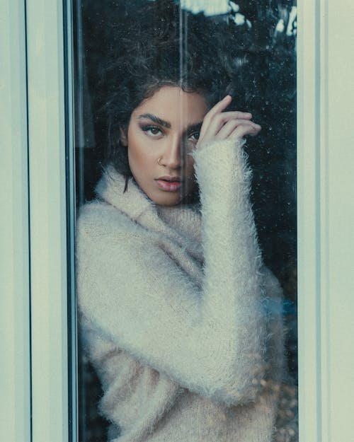 Woman in White Knitted Sweater Standing Behind A Glass Window