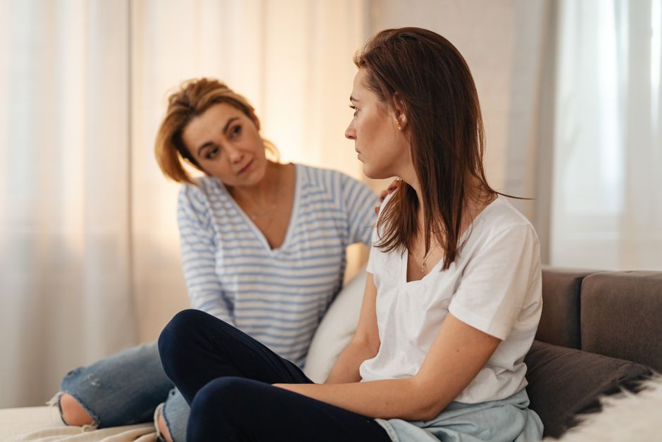 Two women having a heartfelt conversation on a couch, showing empathy and support.