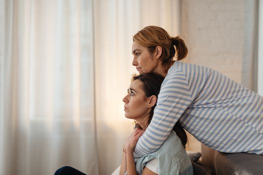 Two women share a comforting embrace, depicting warmth and support in an indoor setting.