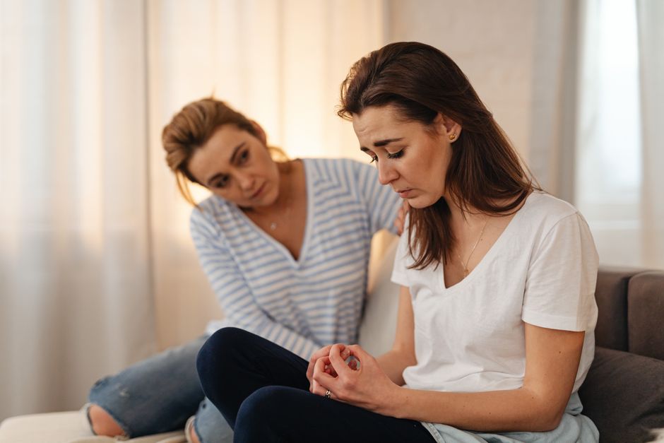 Two women sitting on a couch, sharing emotional support and connection in a warm living room setting.