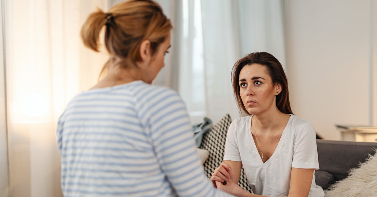 Two women engaged in a serious conversation, sitting indoors with a blurred background.