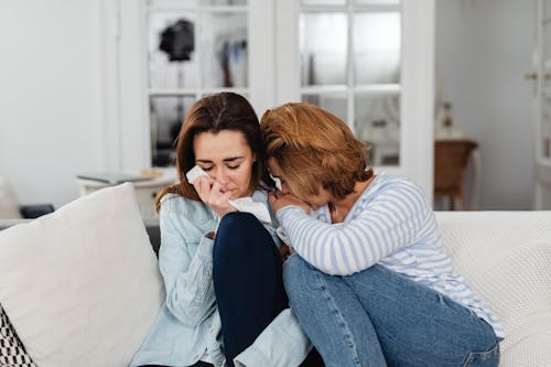 Free Two Women Sitting On White Sofa Crying Together Stock Photo