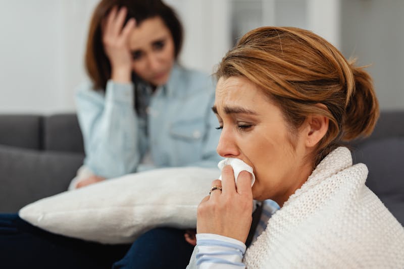 Two women sitting on a couch, expressing and sharing emotions of sadness and support.
