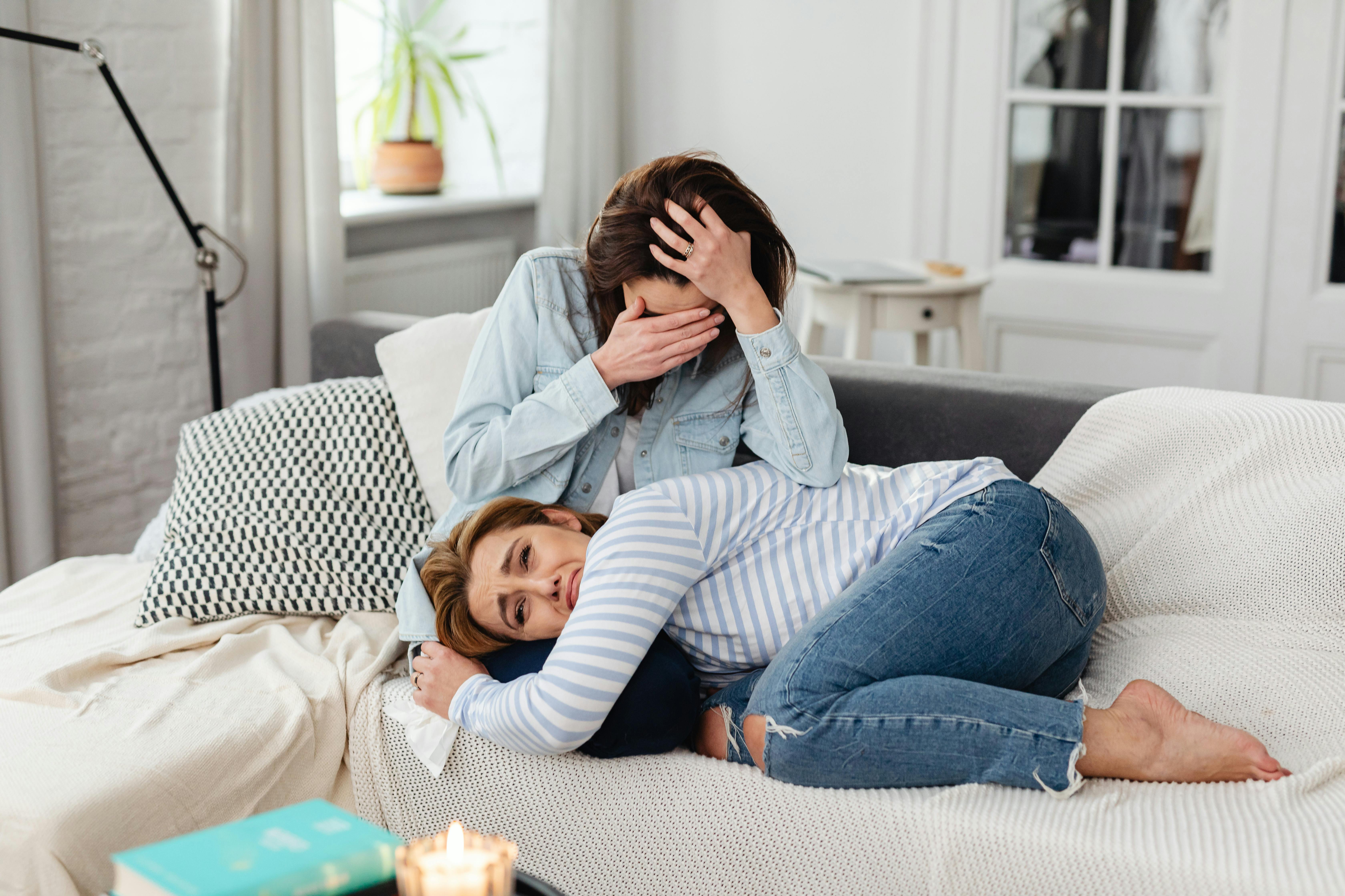 Two women expressing emotions on a sofa, showcasing empathy and companionship.