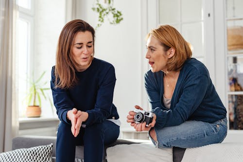 Photo of Woman Holding a Camera while Talking to Her Friend
