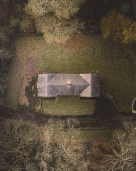 Top-down drone view showing a house amidst green surroundings, highlighting its roof and nearby trees.