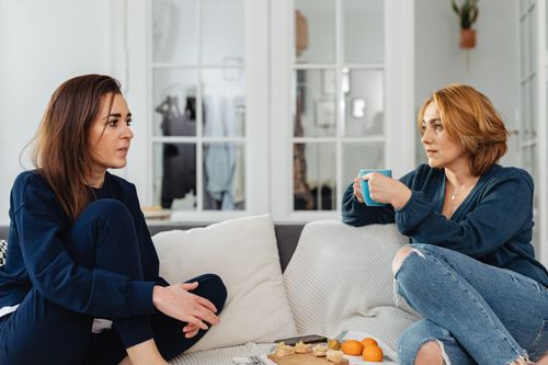 Free Two women enjoying a casual conversation on the couch, sipping tea and snacking indoors. Stock Photo