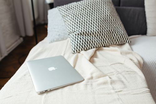 Free A minimalist scene of a laptop on a textured bed with pillows, capturing a relaxed and modern atmosphere. Stock Photo