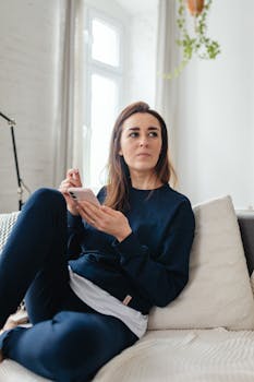 Casual portrait of a woman lounging on a sofa, holding a smartphone indoors.