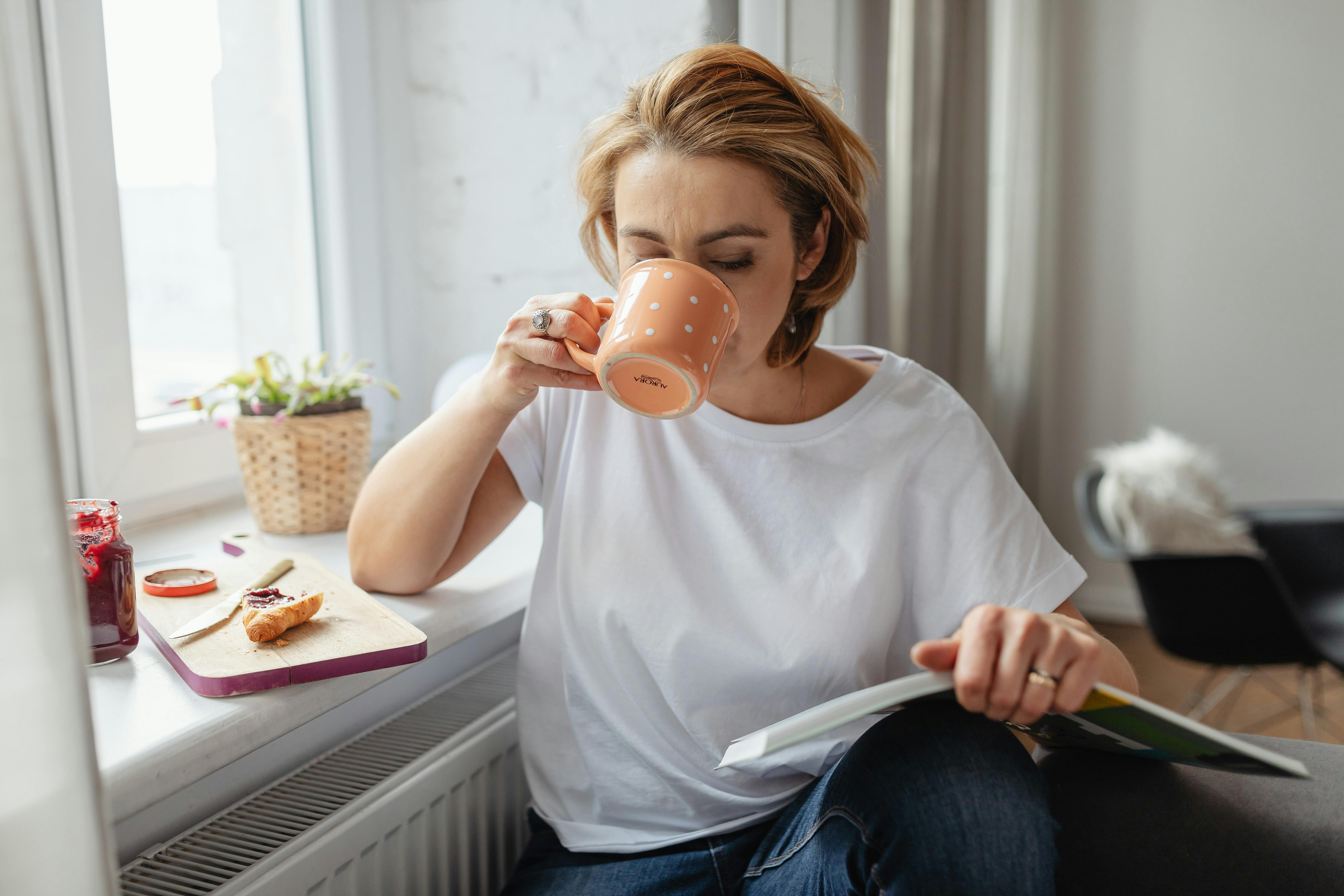Woman Drinking Coffee while Reading Book