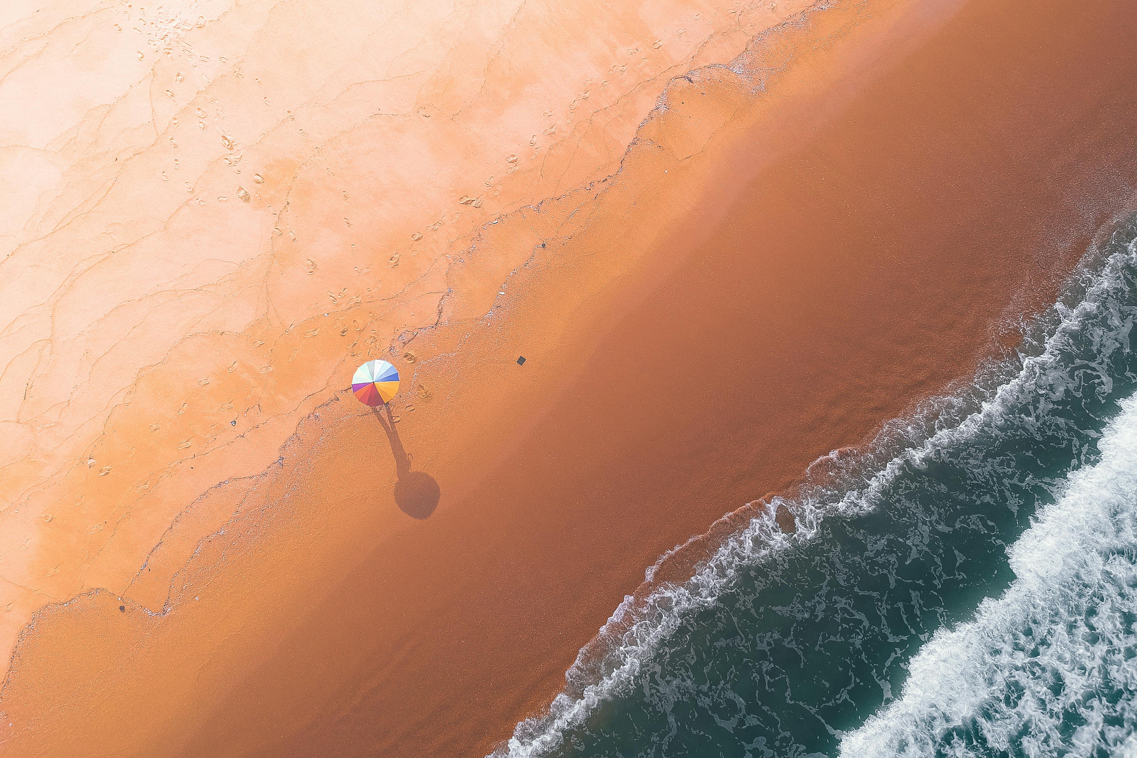 Aerial view of sandy beach with colorful umbrella in middle near wavy water in summer sunny day