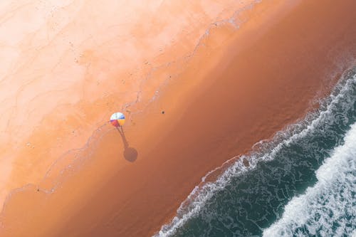 Aerial view of sandy beach with colorful umbrella in middle near wavy water in summer sunny day