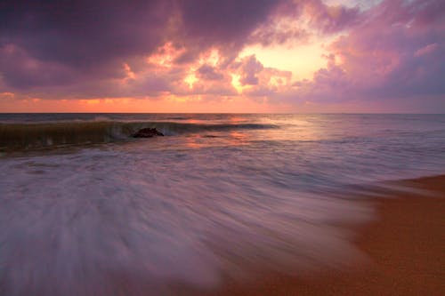 Spectacular seascape of wavy ocean near sandy beach under bright sunset in summer time