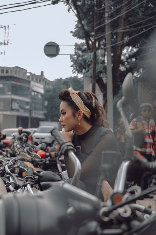 Side view of Asian female in stylish clothes sitting on motorcycle near busy road