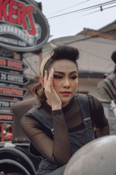 Young Asian female wearing grunge pin up styled outfit sitting in automobile garage
