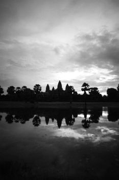 Black and white scenery of calm lake shore with lush thick forest reflecting in still water on cloudy day