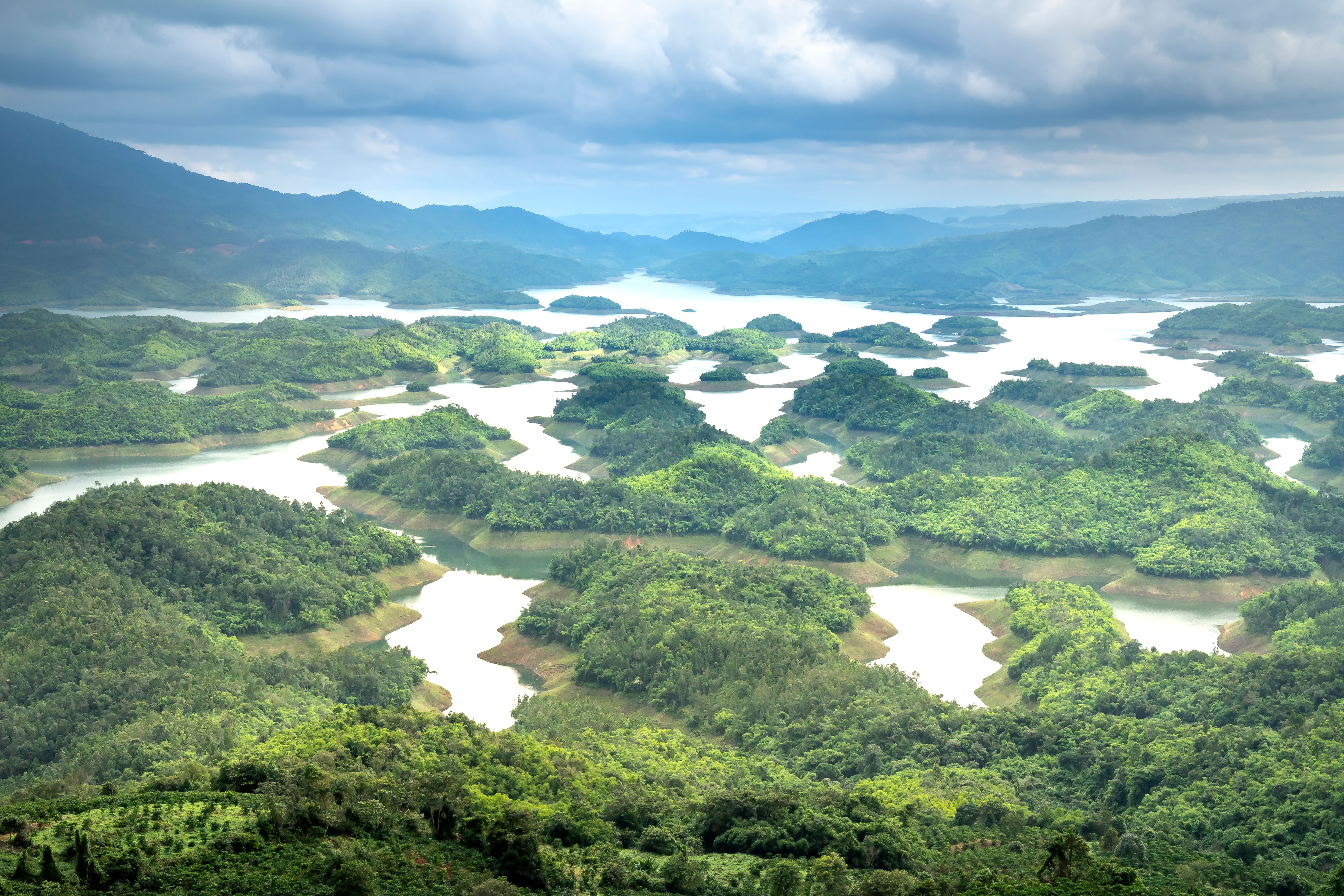 [ColoSach]-curvy-river-flowing-through-hills-covered-with-green-trees-against-mountain-ridge-and-cloudy-sky-in-nature-on-summer-day