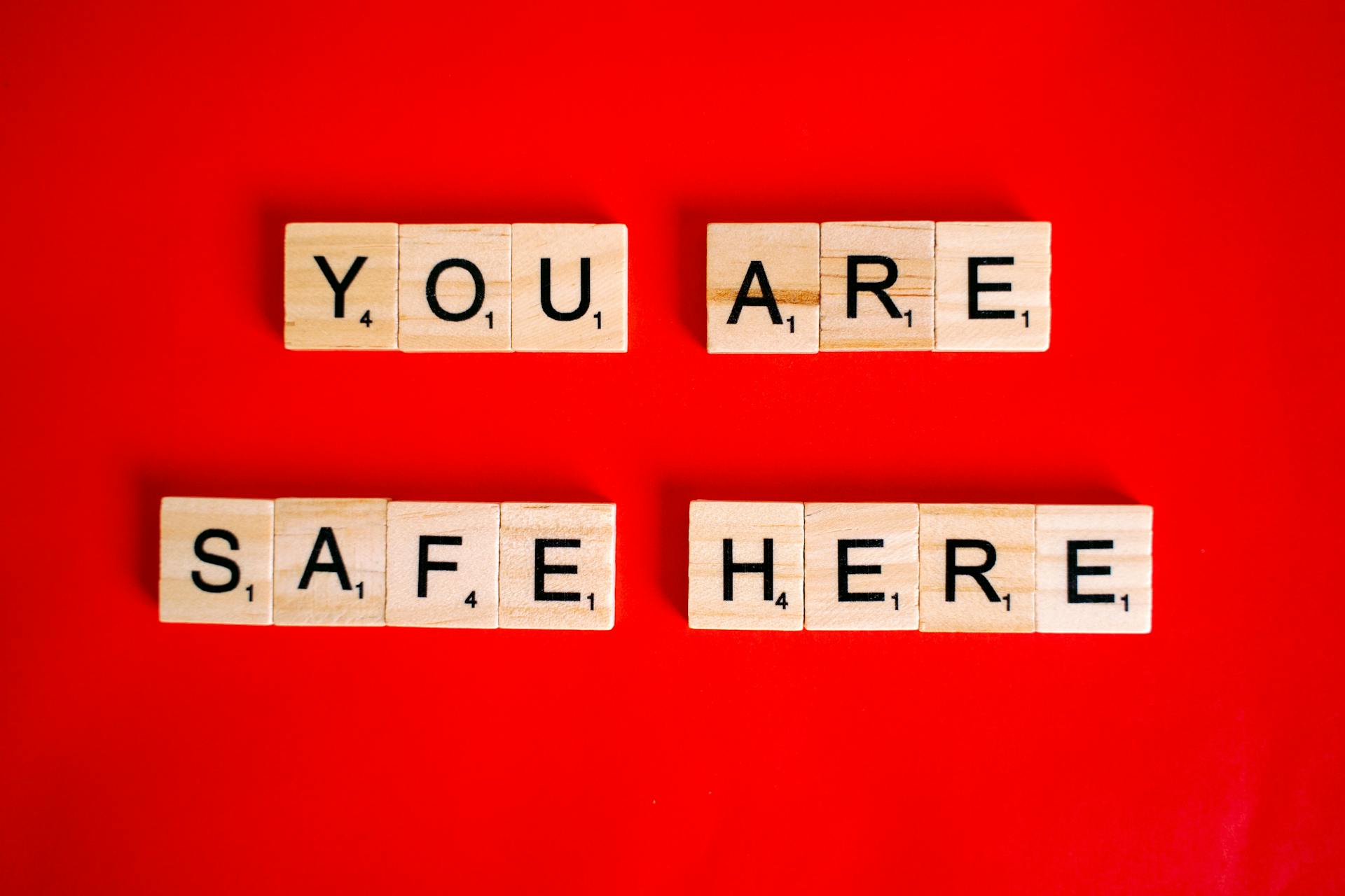 Wooden Scrabble tiles display 'You Are Safe Here' against a red background, symbolizing safety.