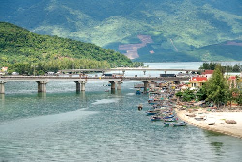 Scenic view of bridges above vast rippling river connecting abundant hilly shores near rural port in exotic country
