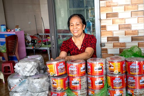 Smiling ethnic vendor against containers with rice cakes