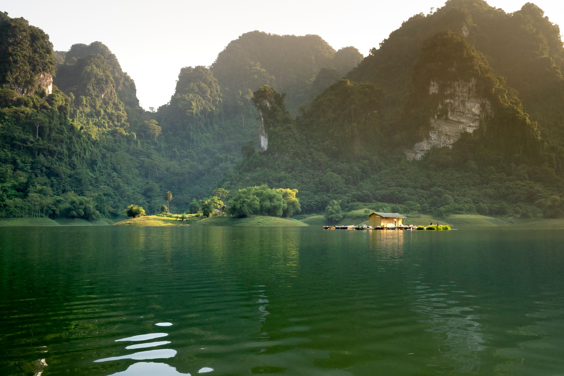 Spectacular view of construction between rippled lake and magnificent mounts with lush green trees in countryside