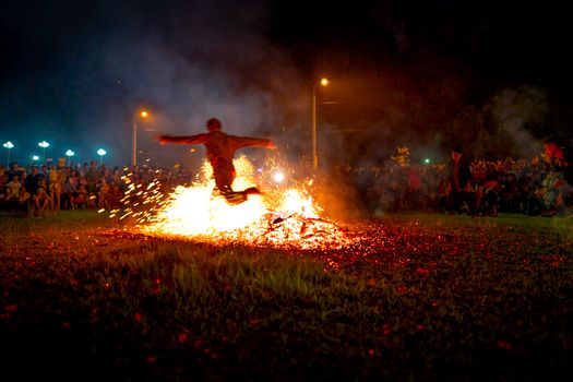 Unrecognizable dancer jumping over fire during night show against spectators