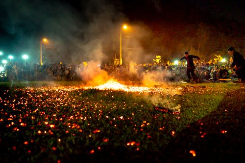 Free Ethnic male fire performers dancing on lawn with flame and smoke against anonymous spectators during show on lawn Stock Photo