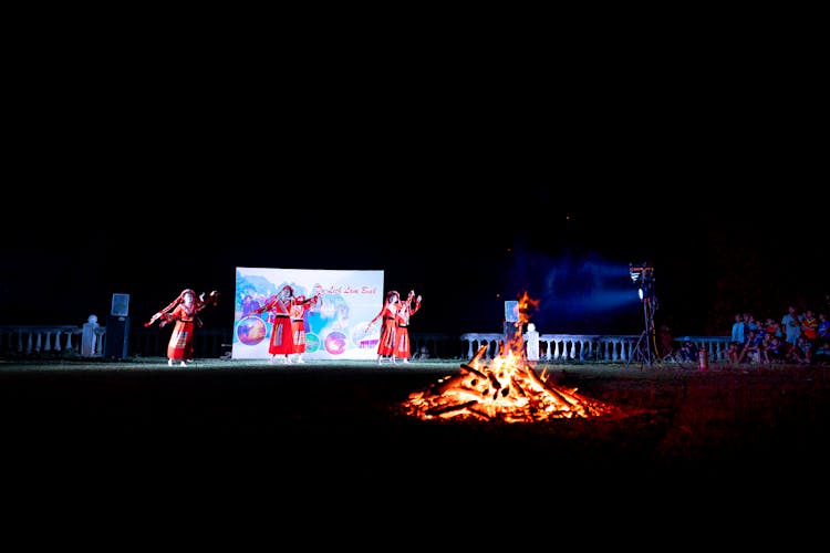 Unrecognizable Women Dancing On Stage Near Fire During Traditional Event At Night