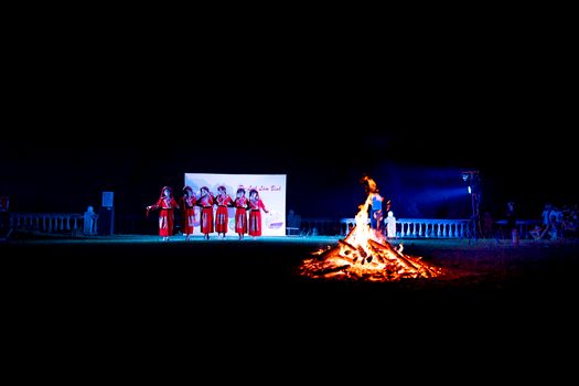 Group of anonymous women in costumes dancing on stand near fire during traditional festival at night in Vietnam